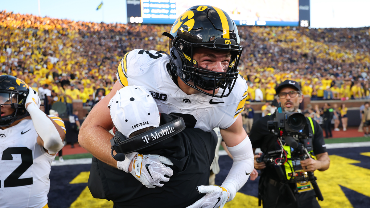 Iowa player in a black and yellow helmet embraces a staff member on the field after a game.