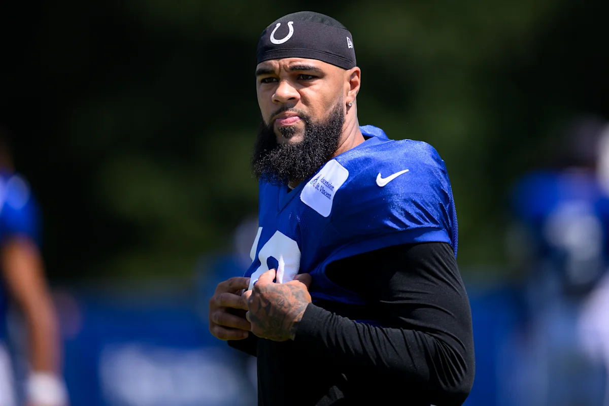 Football player in blue Colts jersey and black head covering stands during practice.