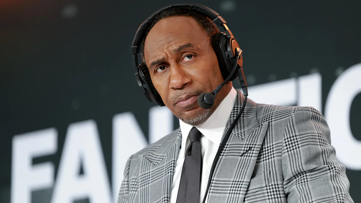 Stephen A. Smith wearing a headset and gray plaid suit during a broadcast.