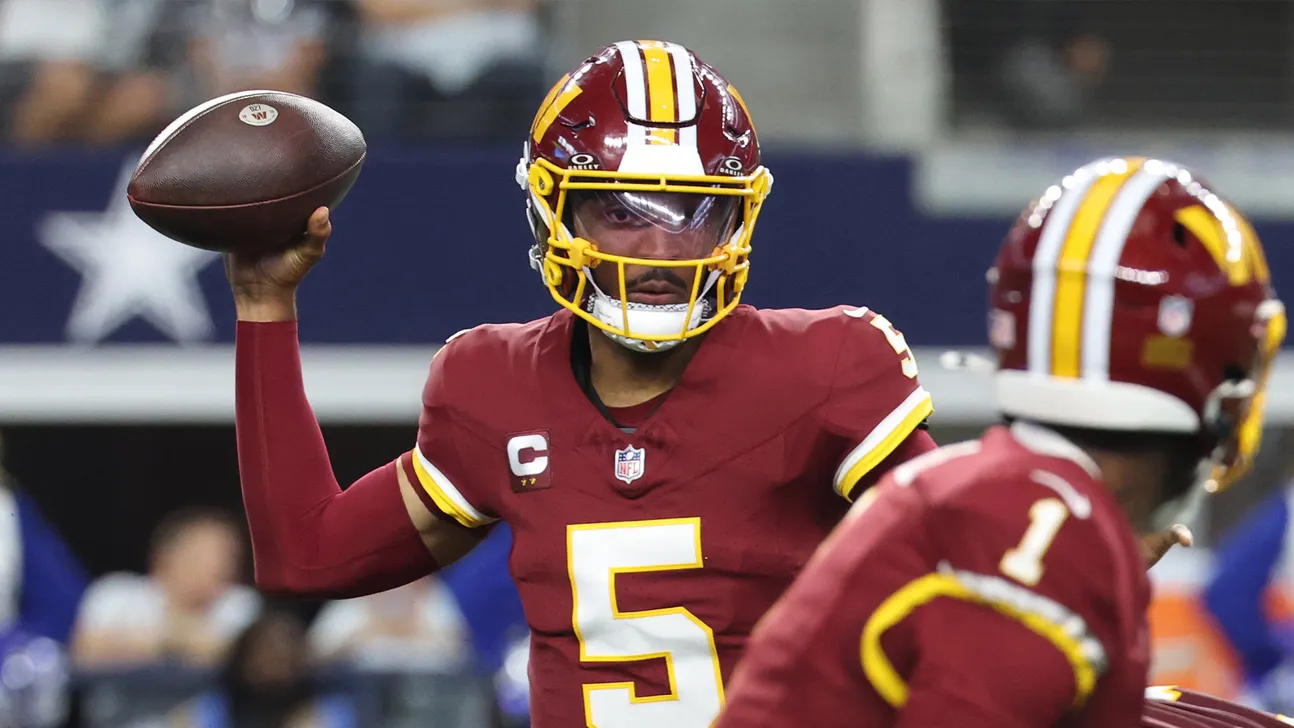 A Washington quarterback in burgundy and gold prepares to throw during a game.