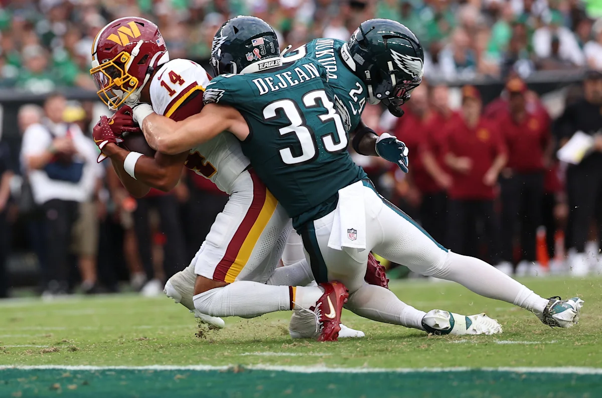 Football players in burgundy and green uniforms collide during a tackle near the end zone.