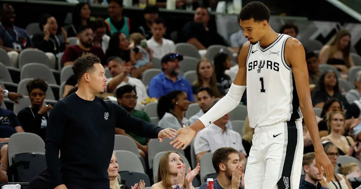 A Spurs player in a white number 1 jersey reaches down to greet a man in black courtside.