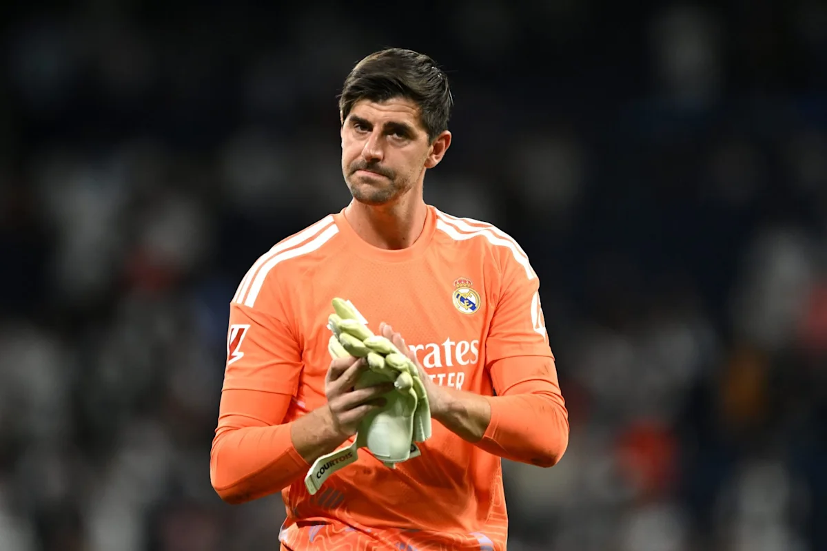 Goalkeeper in orange Real Madrid kit claps while holding gloves during a football match
