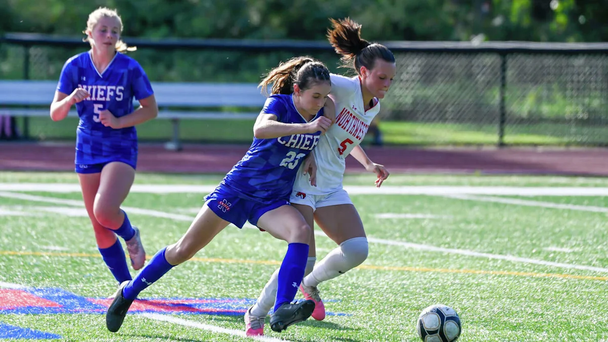 Two girls in blue and white soccer uniforms sprint for the ball during a game.