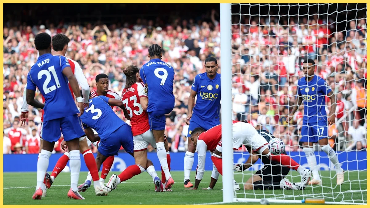 Footballers in blue and red kits contest the ball near goal during a match