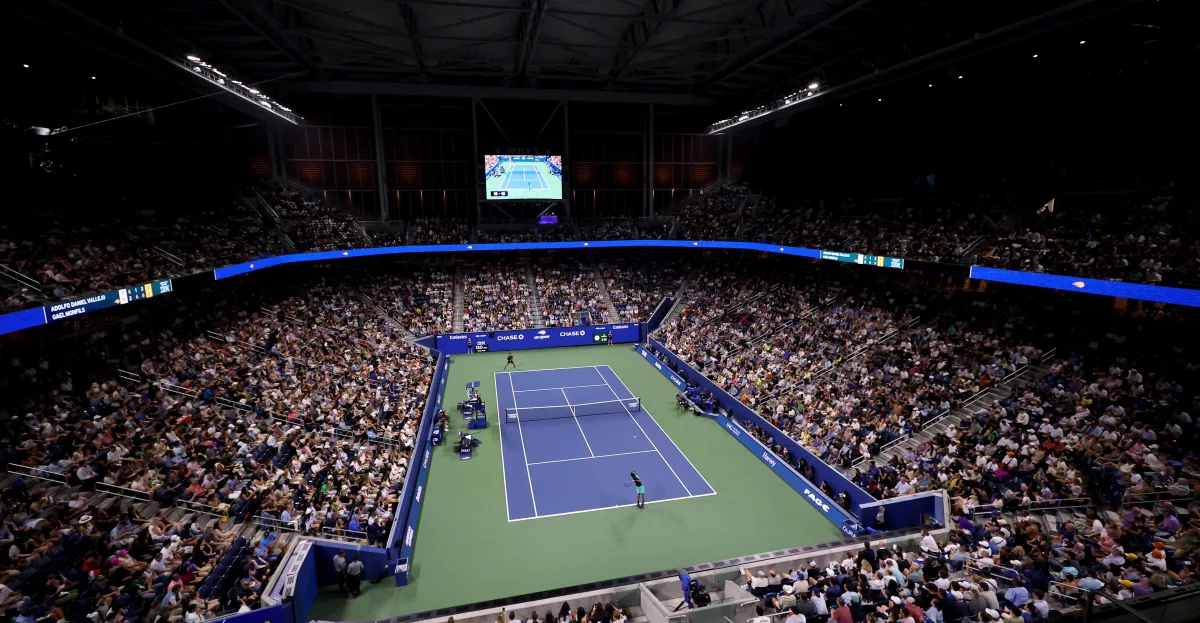 A packed indoor tennis arena surrounds players competing on a blue and green court.