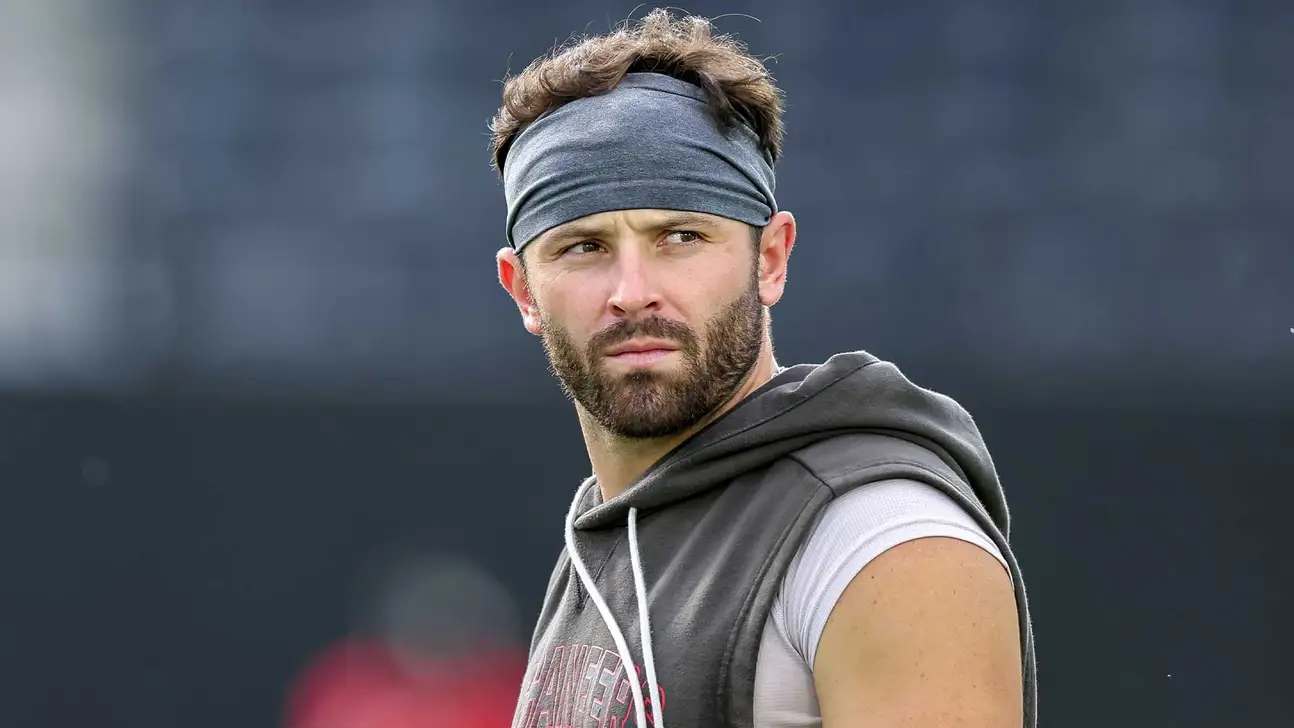 Football player wearing a gray headband and sleeveless hoodie looks off-camera.