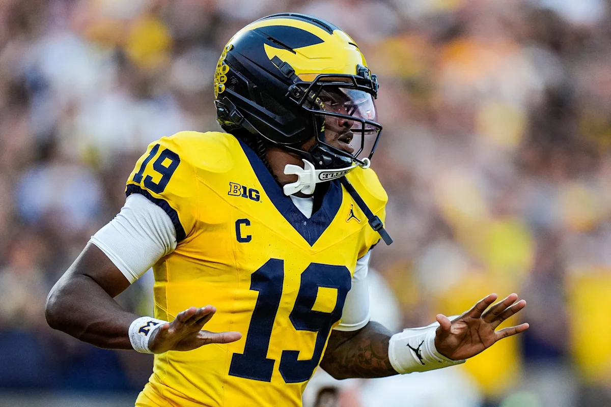 Michigan football player wearing number 19 jersey and helmet extends both hands during a game