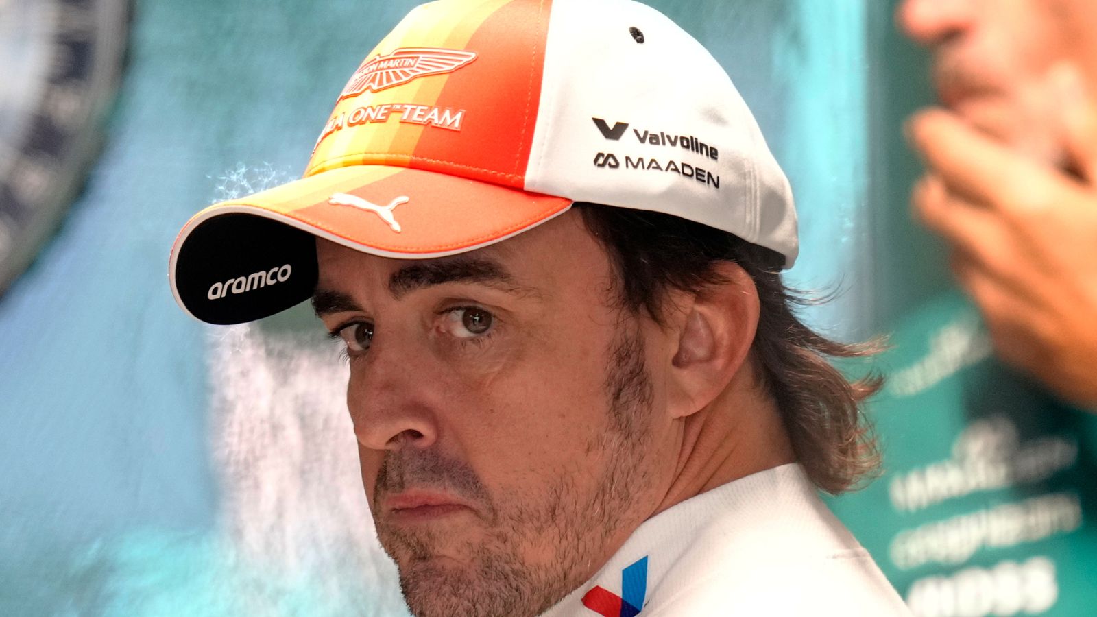 Formula One driver wearing Aston Martin cap and team shirt, looking toward the camera