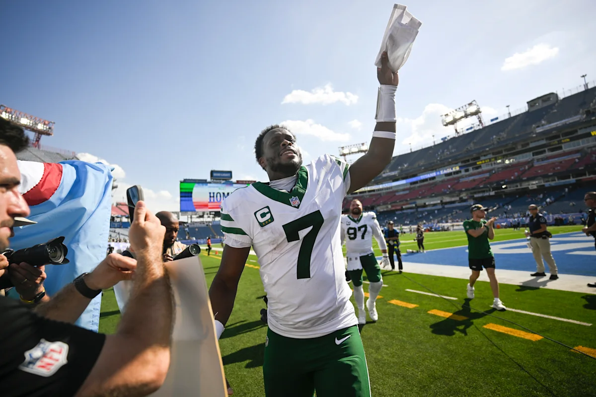 New York Jets player raises a football while walking across the field after a game