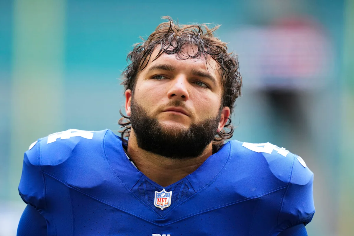 Bearded football player in blue jersey looks off-camera with a serious expression