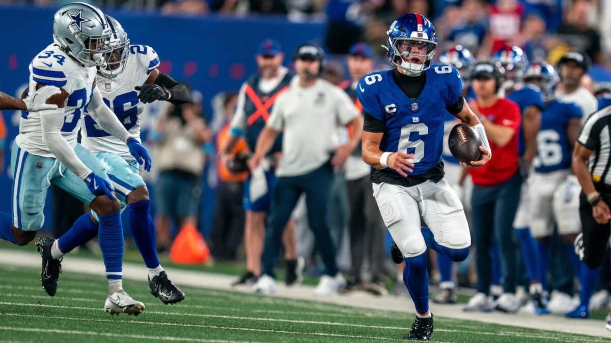 Giants quarterback runs with the ball as Cowboys defenders pursue during a football game.