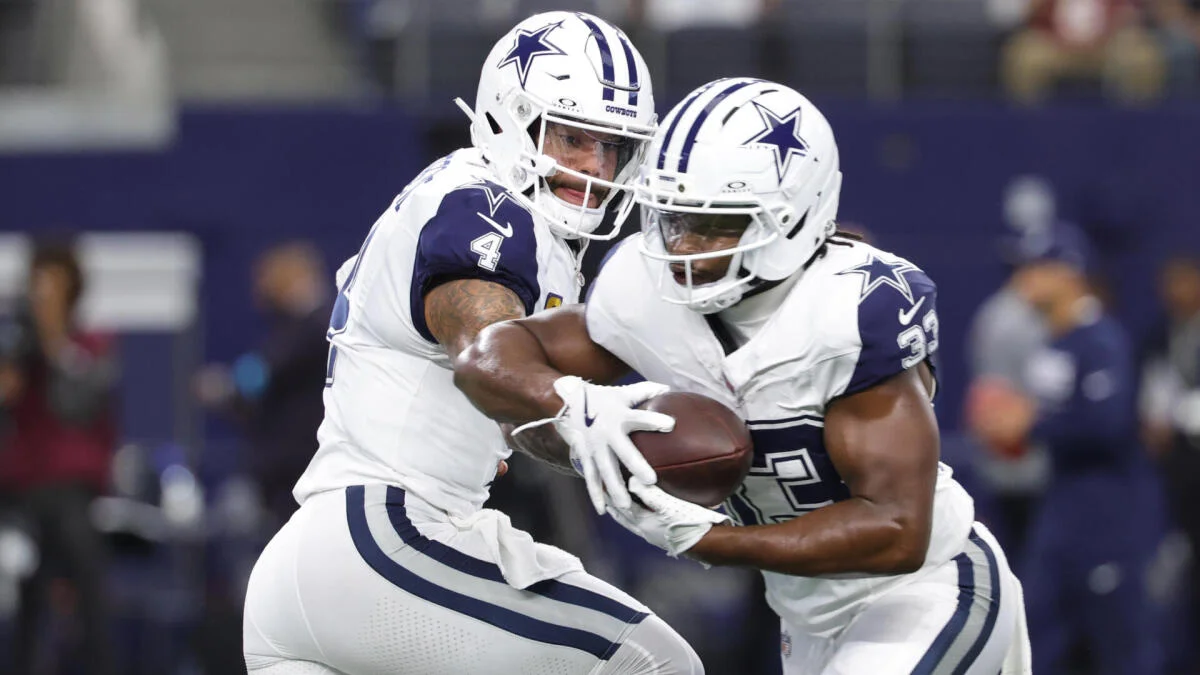 Two Dallas Cowboys players in white uniforms exchange a football during a game.