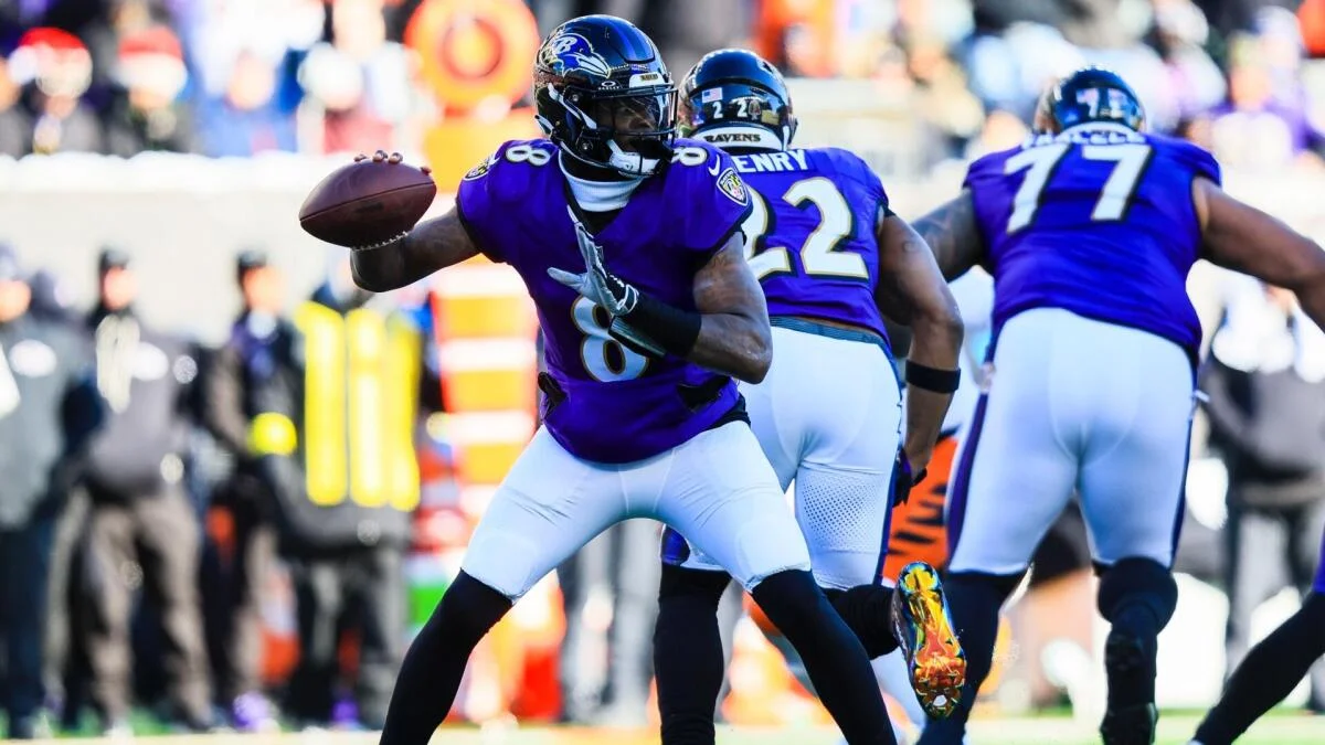 A Ravens player holds the football as teammates in purple uniforms line up behind him.