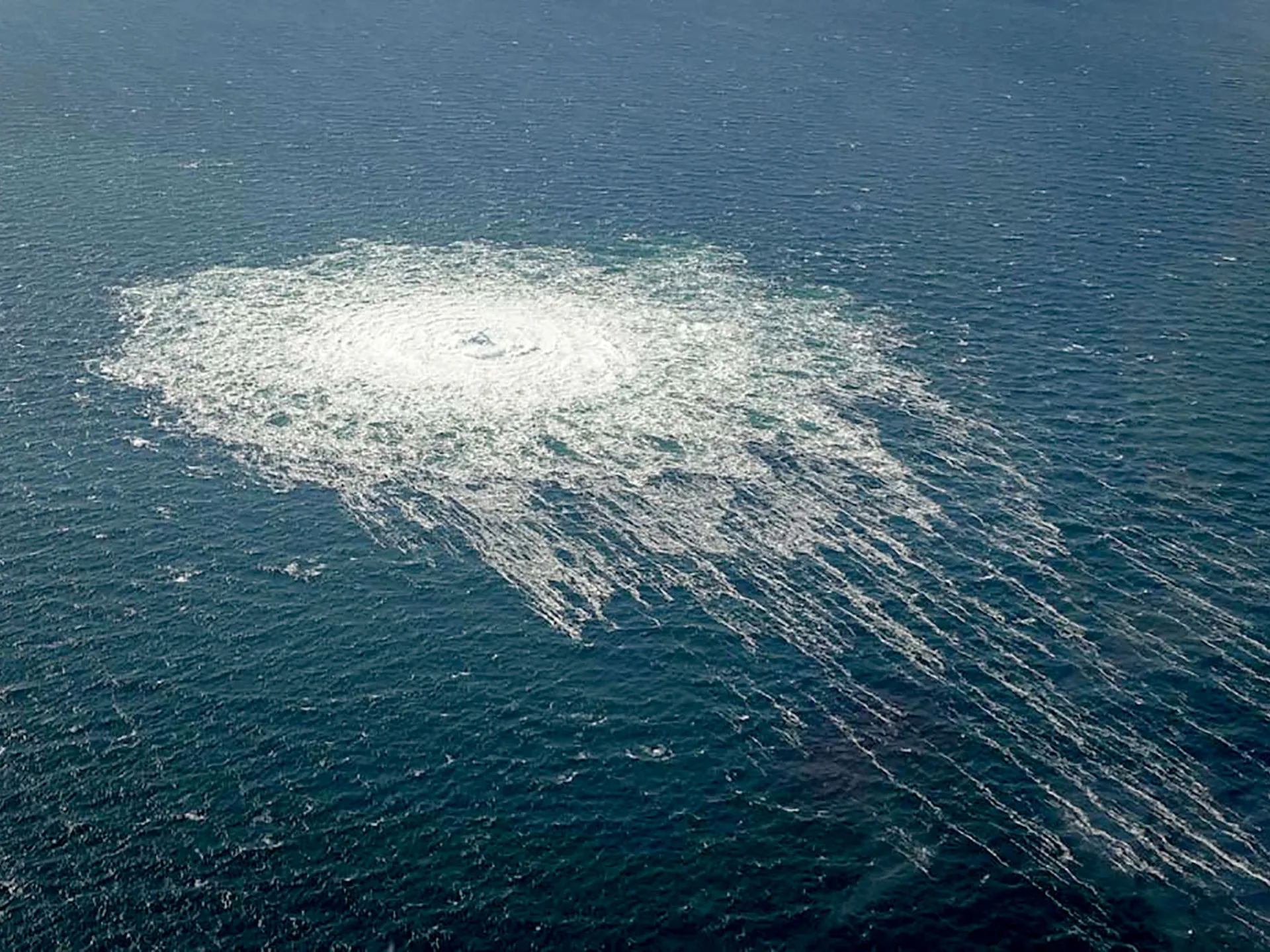A broad patch of white foam spreads across dark blue water, with streaks trailing toward the lower right.