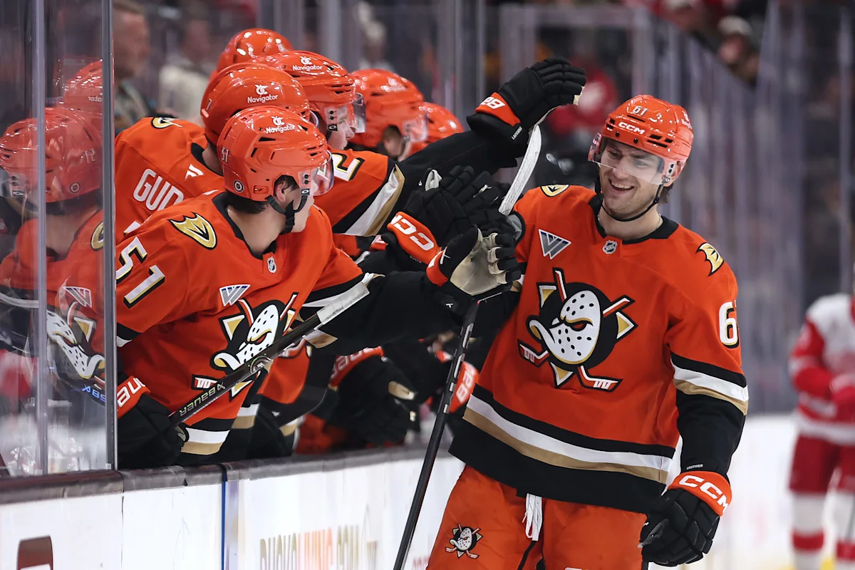 Anaheim Ducks hockey players in orange jerseys celebrate with a teammate during a game.