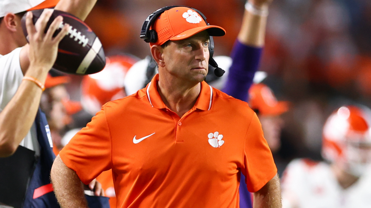Football coach in orange Clemson polo and headset standing on sideline during a game