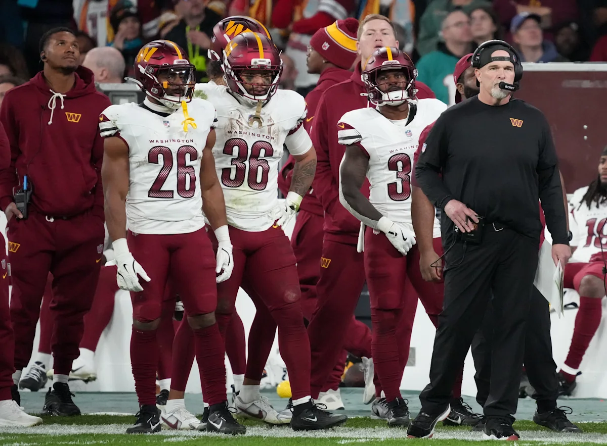 Washington football players and staff stand together on the sideline during a game.