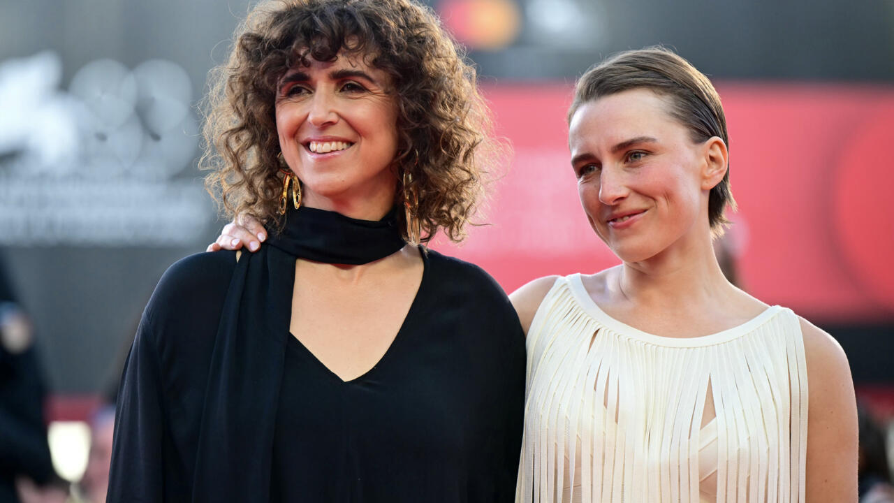 Two smiling women pose together on a red carpet, wearing black and cream dresses.