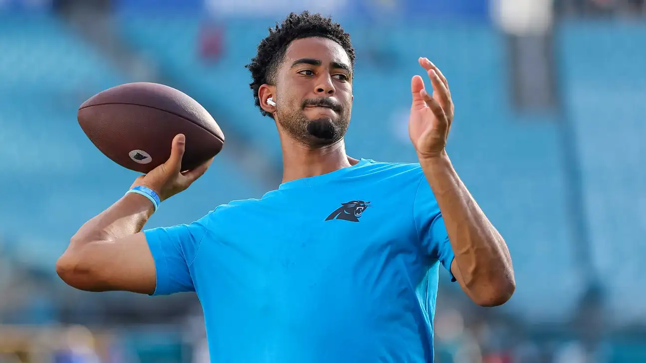 Football player in blue shirt holds a football during a passing motion.