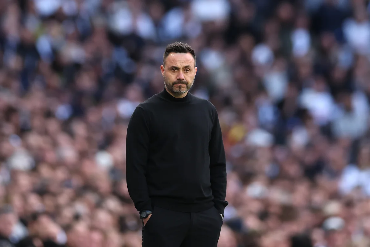 Football manager in black sweater standing on the touchline before a blurred crowd