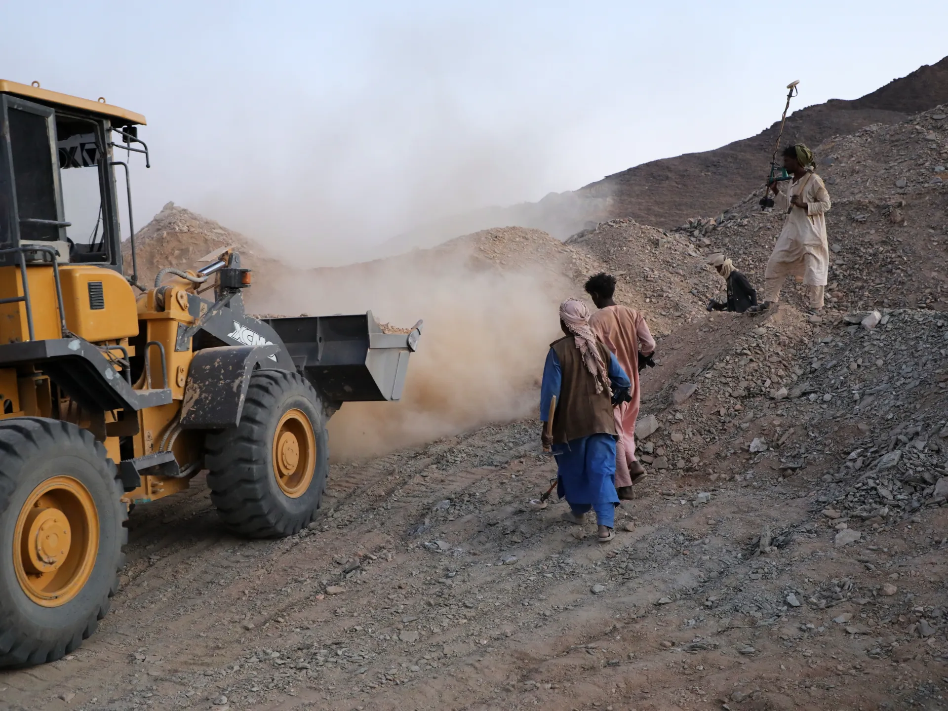 Bulldozer and people stand amid dust and rubble on a rocky mine site.