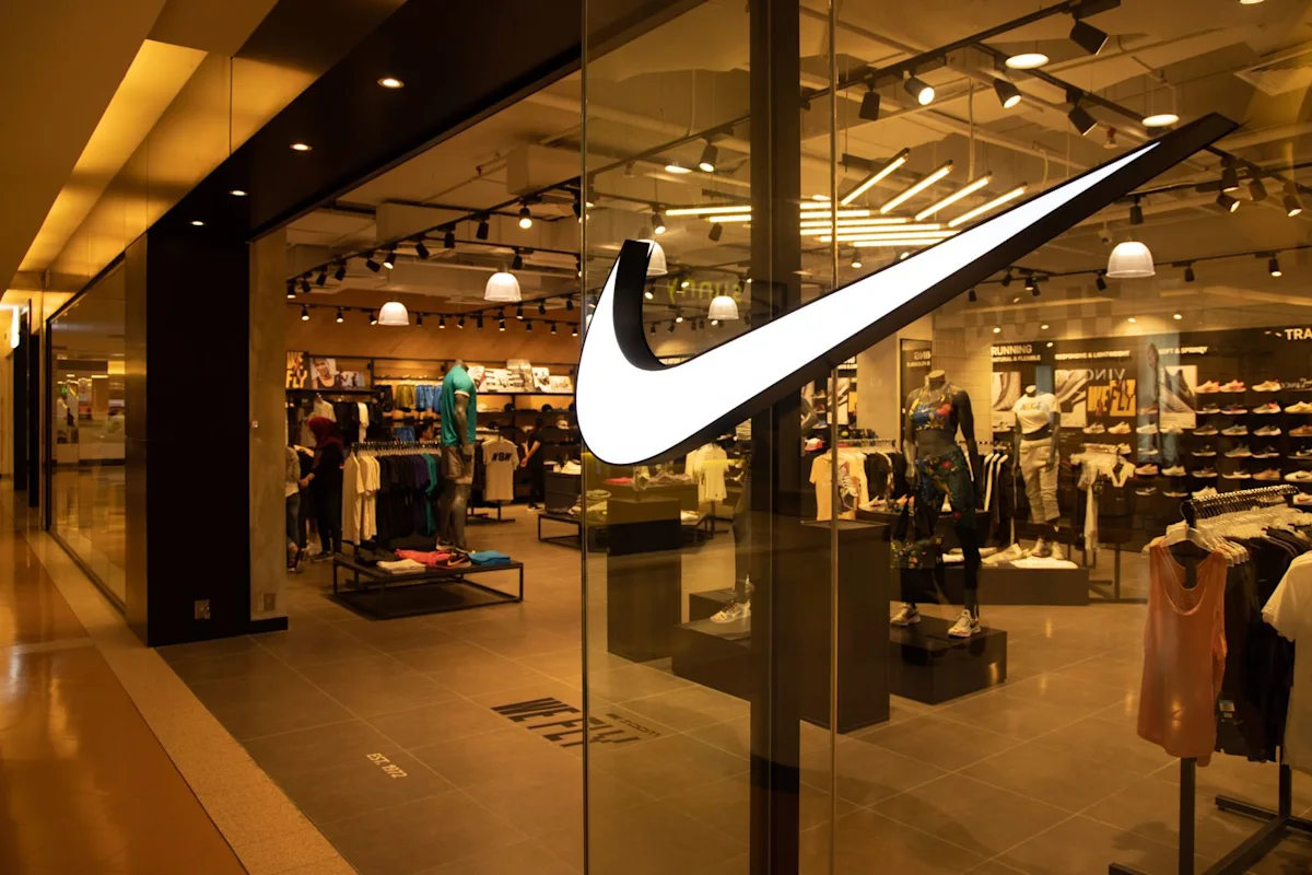 Large white Nike swoosh displayed on glass storefront of a brightly lit athletic apparel store