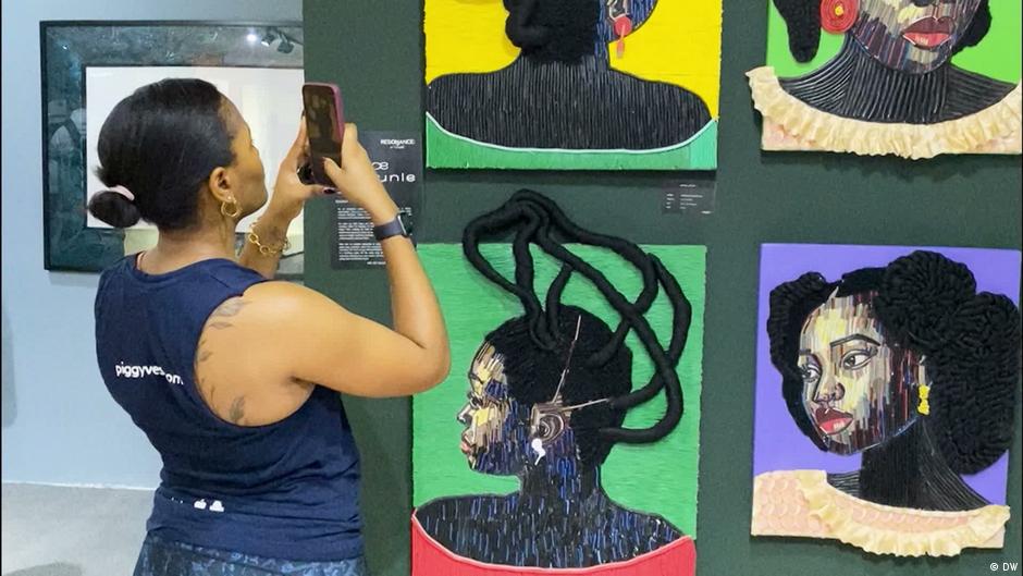 Visitor photographs an exhibition of colorful textile portraits depicting Black women.