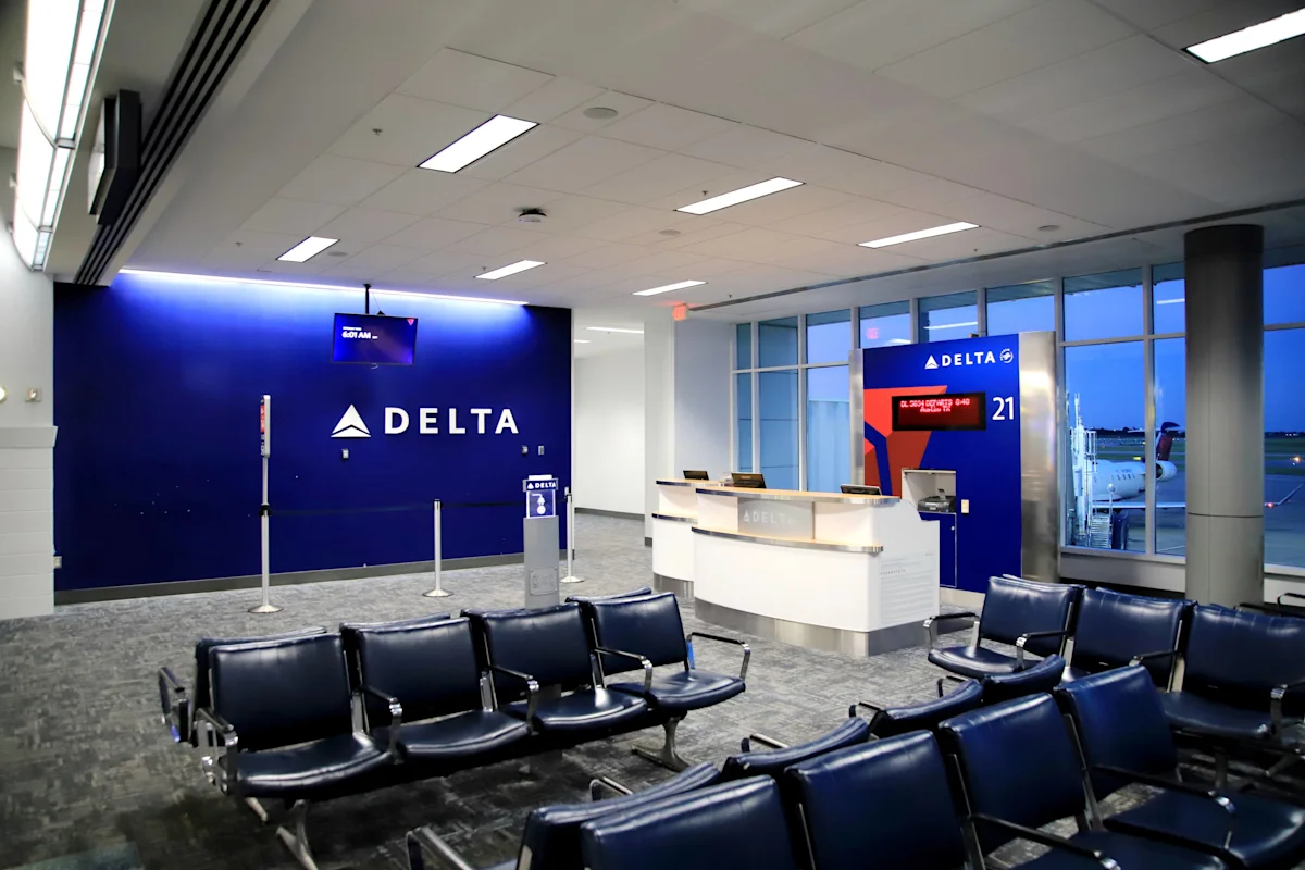 Delta airport gate area with check-in counter, seating, and an aircraft visible through windows.