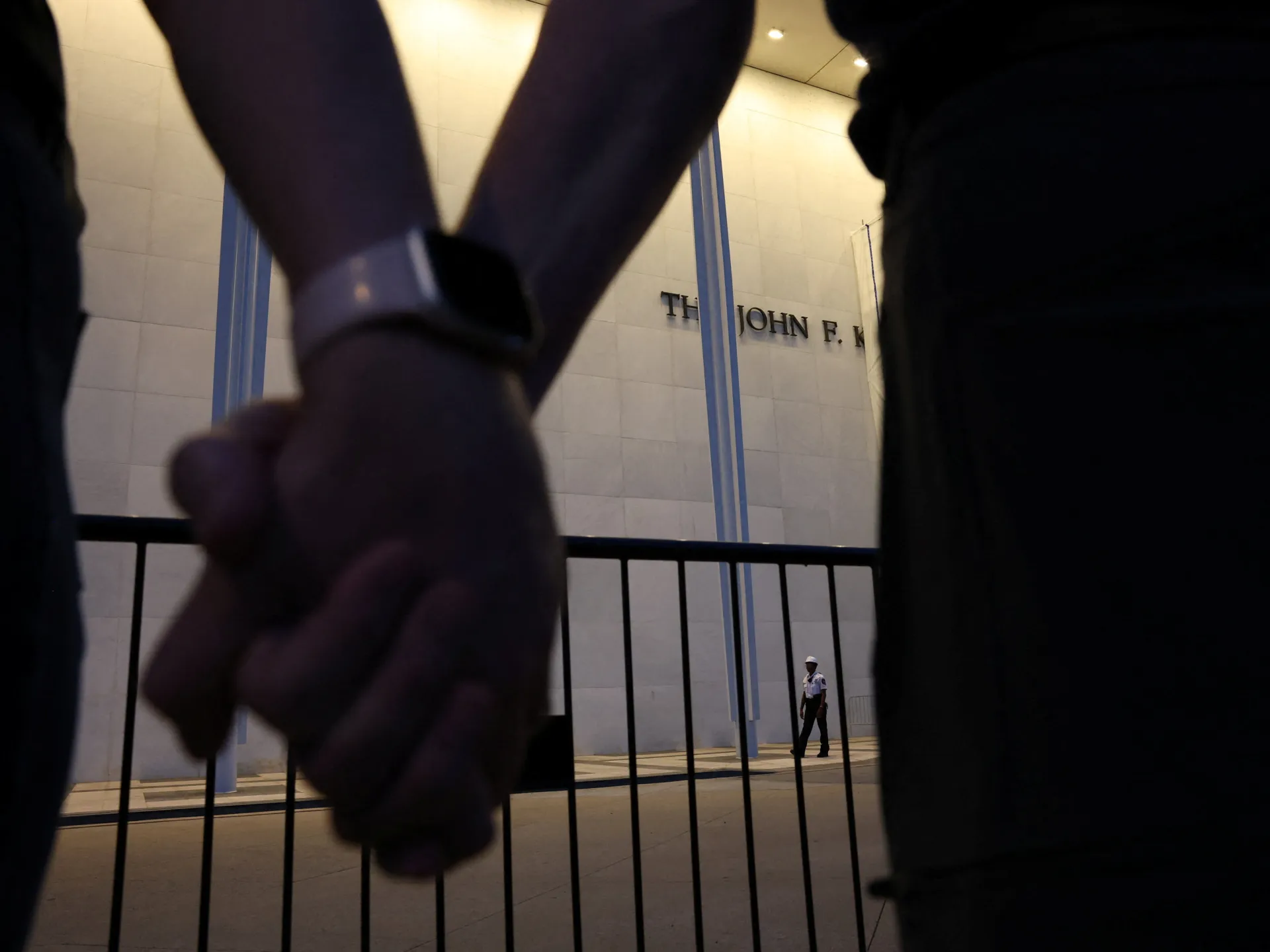 Clasped hands of demonstrators frame the Kennedy Center facade behind a security railing.