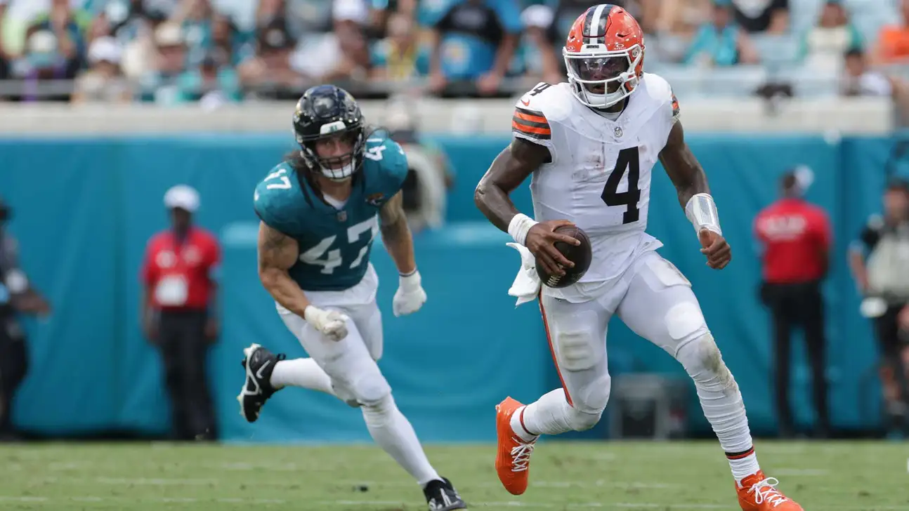 Cleveland quarterback in white uniform runs with football as Jacksonville defender pursues from behind