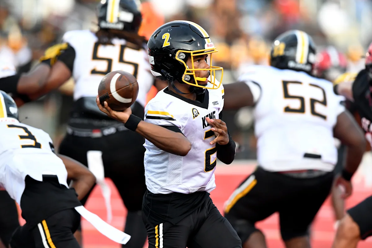 High school football quarterback in black and gold uniform prepares to throw while teammates block around him.