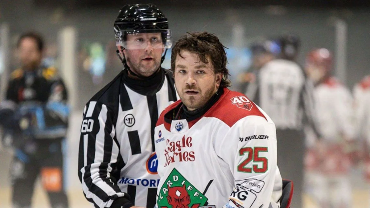 Ice hockey player in a white jersey skates with a referee closely behind him