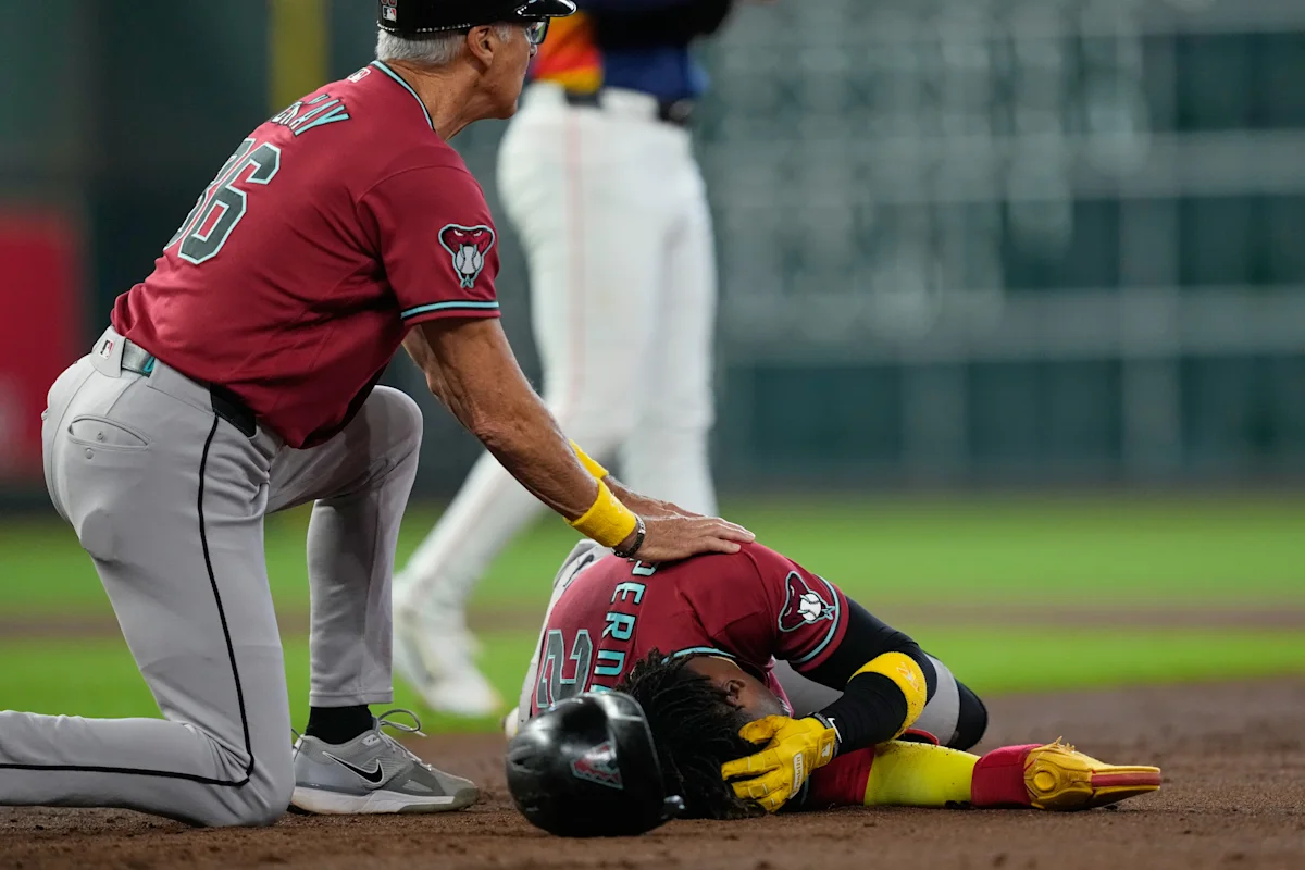 Baseball coach checks on injured player lying on the infield after a play