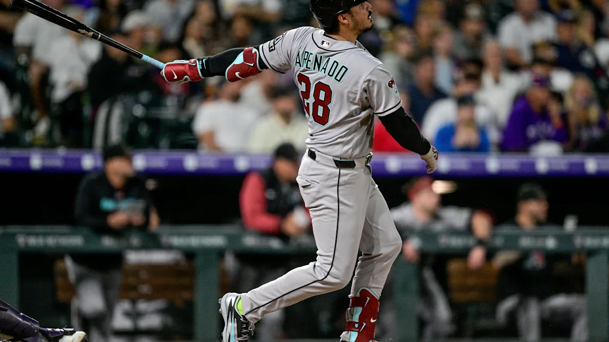 Baseball player in a gray uniform swings a bat, with a blurred crowd behind him.