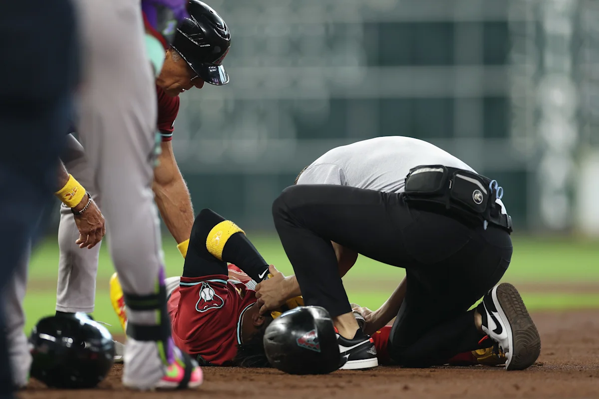 Baseball player lies on dirt as medical staff attend to him during a game.