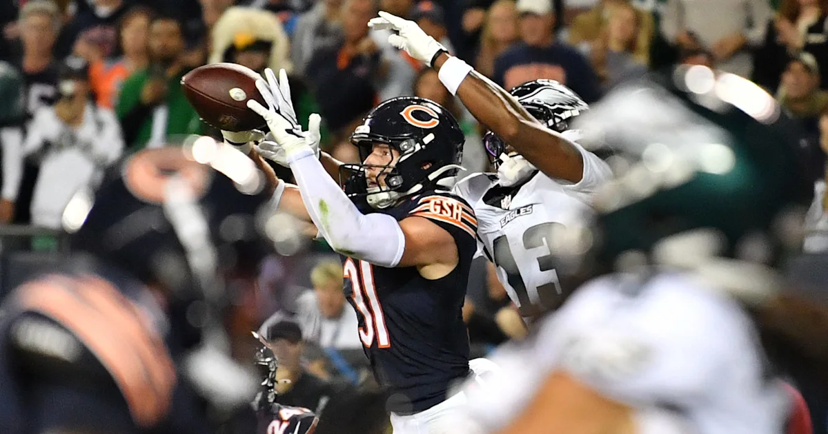 Chicago Bears player reaches for a football as an Eagles defender contests the catch during a game.
