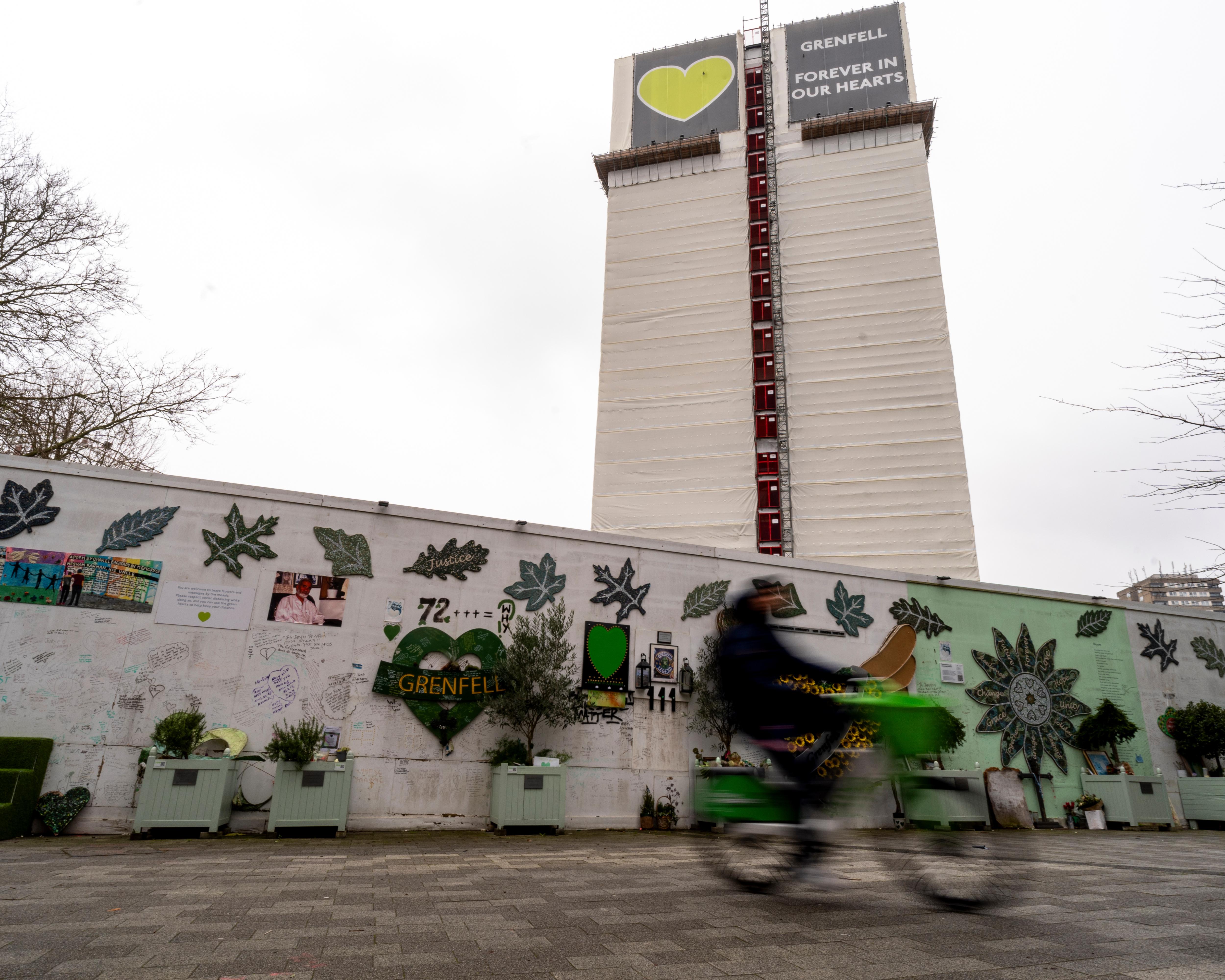 Wrapped Grenfell Tower rises behind a memorial wall covered with messages, artwork and tributes.