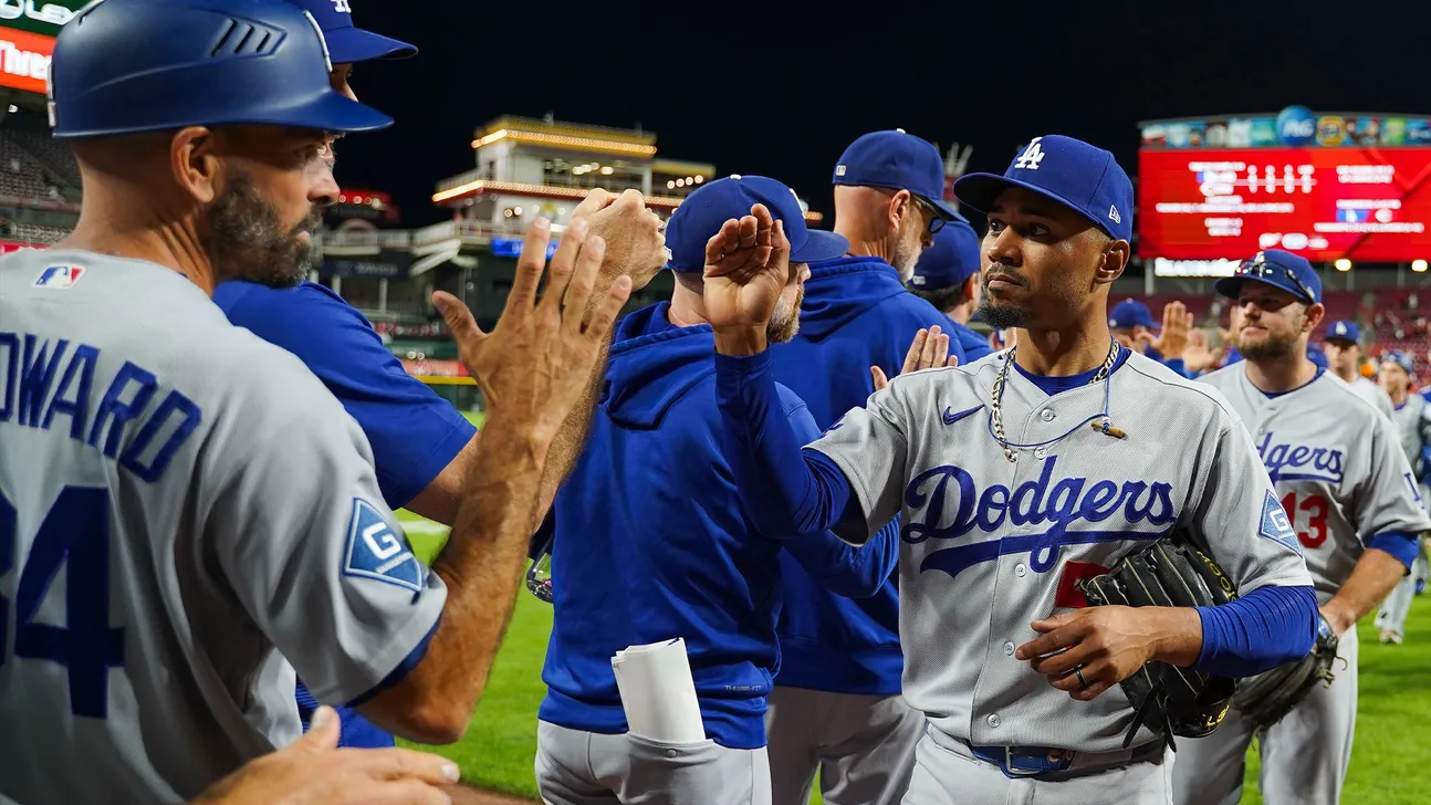 Dodgers players exchange high-fives on the field after a game under stadium lights.