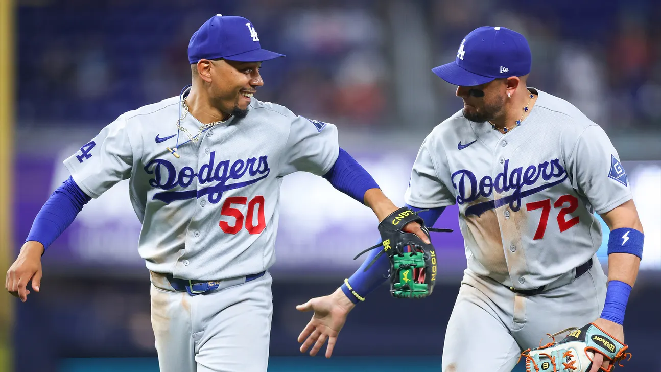 Two Los Angeles Dodgers players in gray uniforms celebrate together on the baseball field.