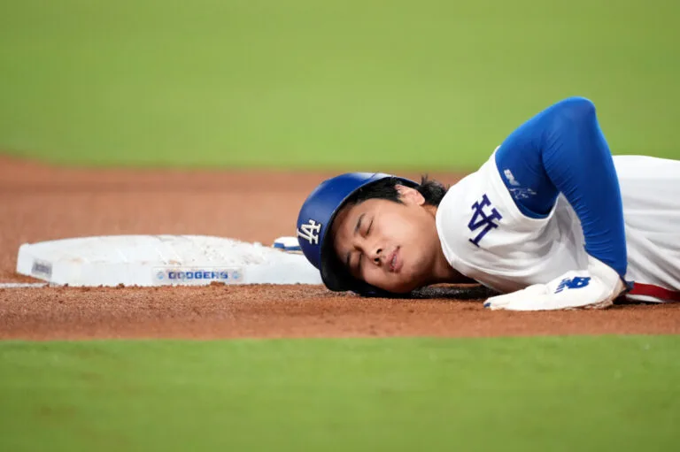 Dodgers player lies on his side beside a base on the baseball field.