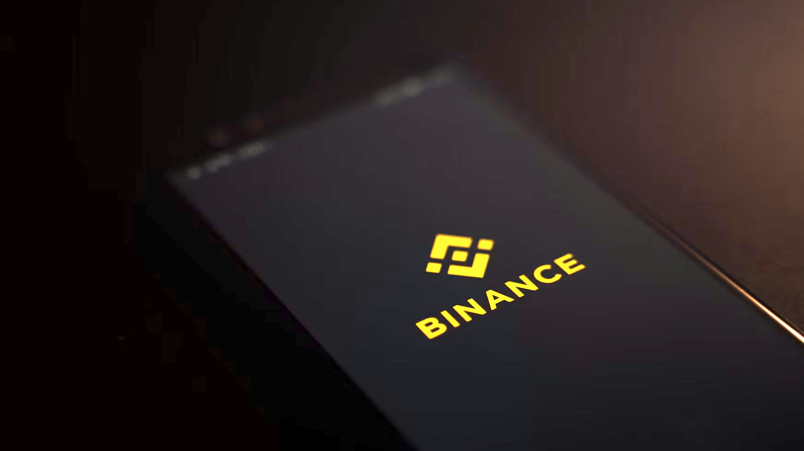 Binance logo and wordmark glowing yellow on a dark device surface