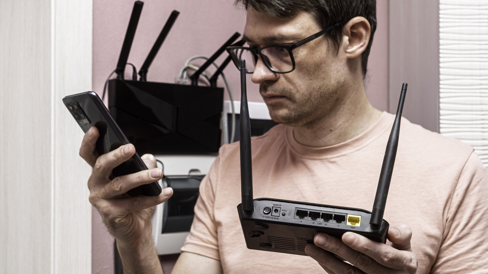 Man examines a smartphone while holding a black Wi-Fi router with two antennas.