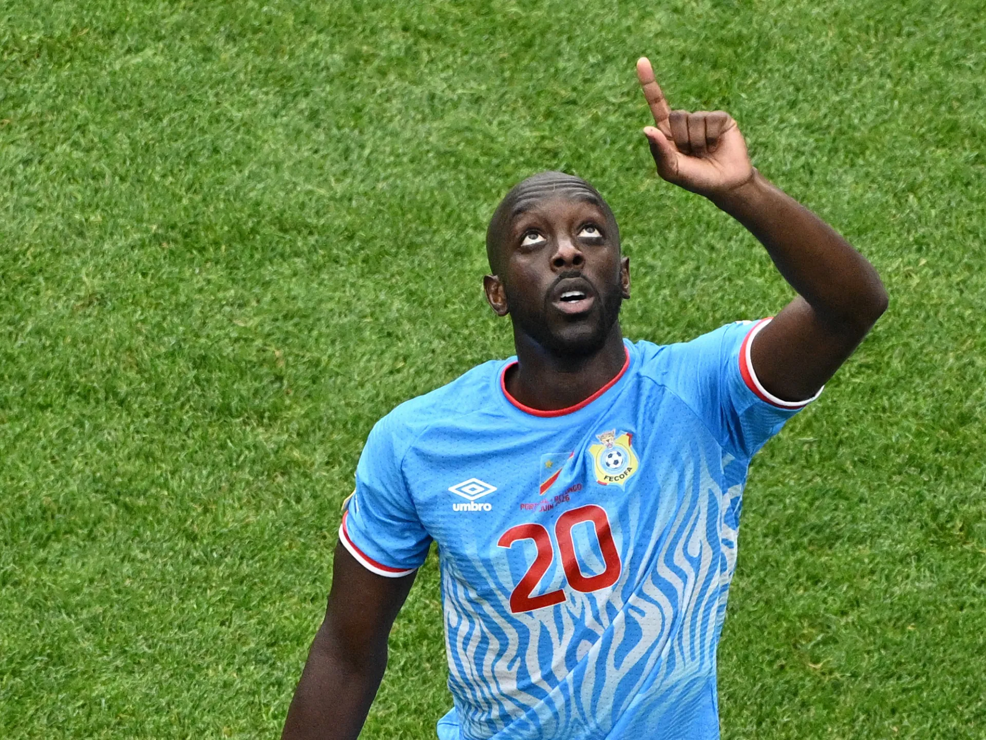 Footballer in a blue number 20 jersey raises one finger while lying on the pitch.