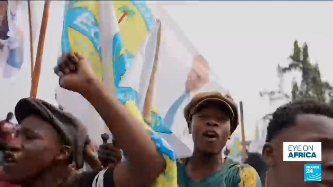 Crowd members raise fists and flags during a street demonstration, with France 24 branding visible.