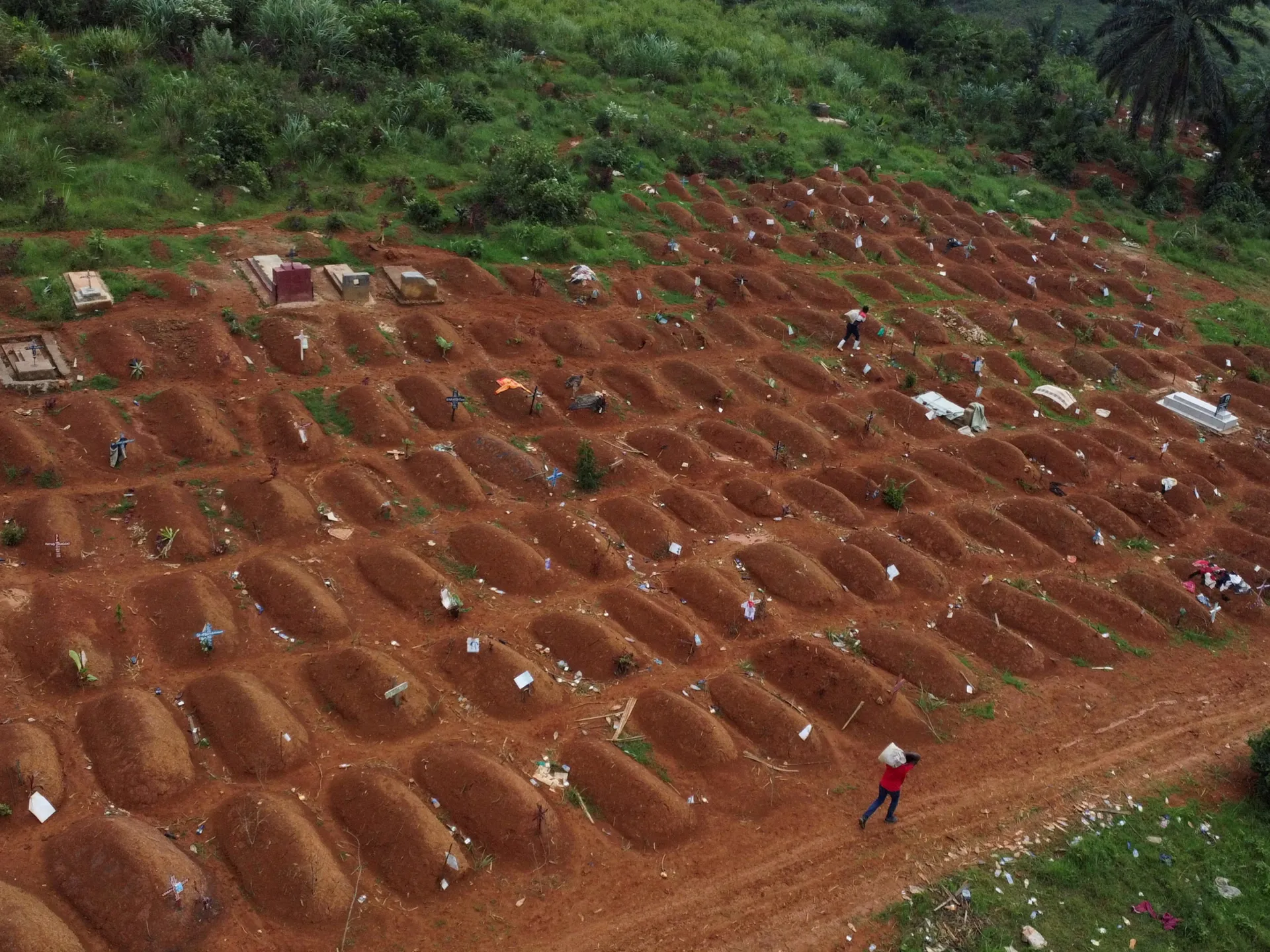 Aerial view of a large cemetery with rows of red-earth graves and people walking among them