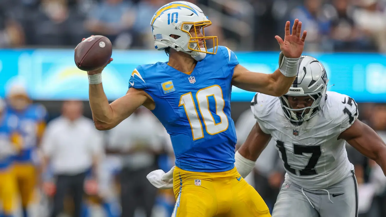 Chargers quarterback in blue and yellow prepares to throw as a Raiders defender closes in.