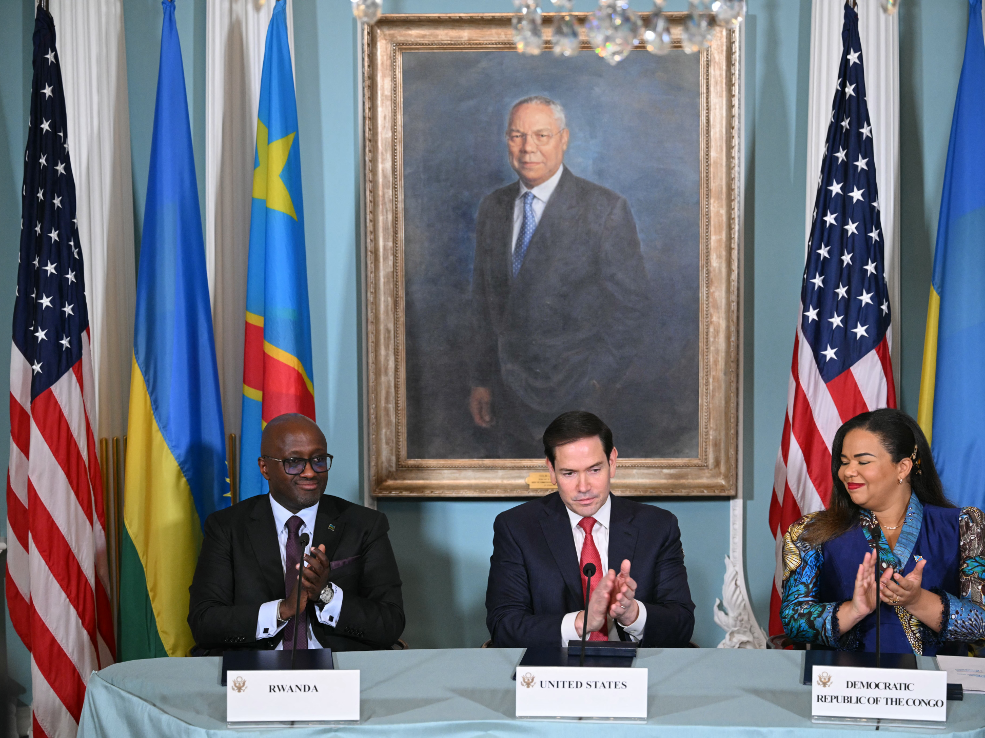 Officials from Rwanda, the United States and Democratic Republic of the Congo sit beneath a framed portrait.