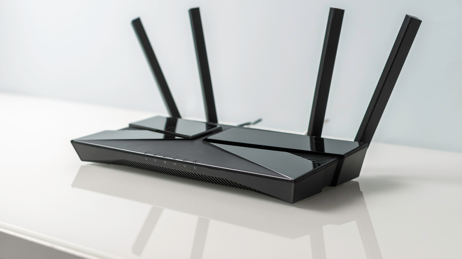 Black wireless router with four upright antennas resting on a white reflective surface