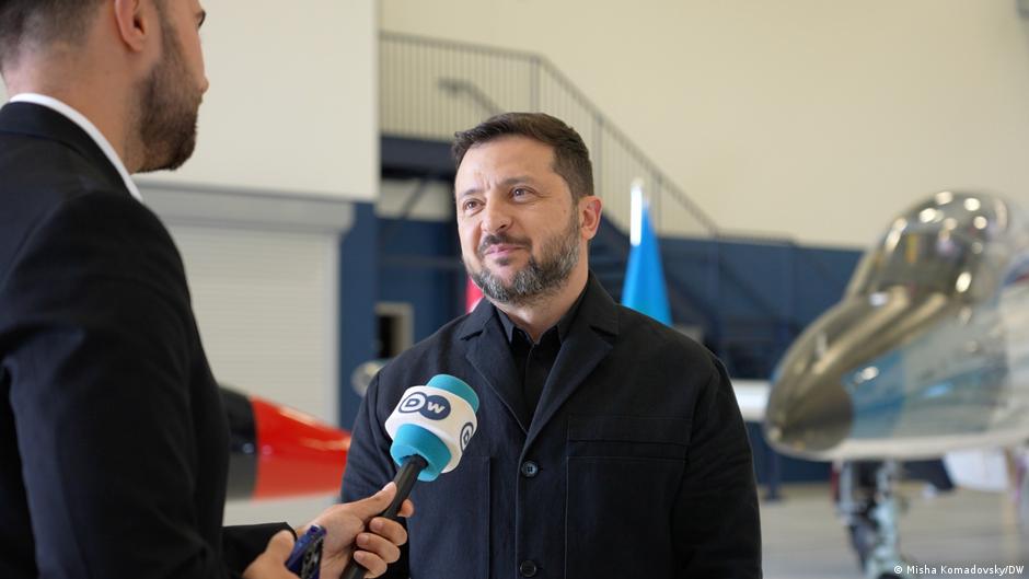 Man in black jacket speaks into a DW microphone inside an aircraft hangar